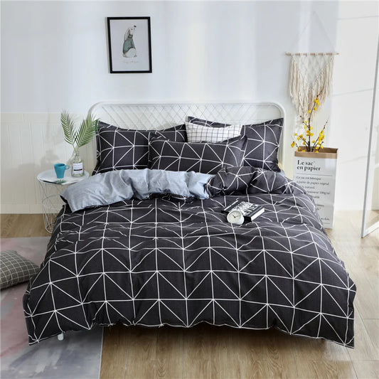 Housse de couette anthracite à motif triangles blancs avec envers gris clair à micro-points, installée sur un lit double dans une chambre contemporaine.