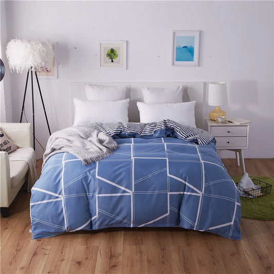 Housse de couette bleue réversible à motif géométrique blanc et revers rayé disposée sur un lit double dans une chambre moderne.
